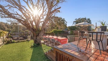 Une terrasse extérieure avec une table à manger pour quatre personnes, entourée de chaises, située sous un grand arbre.