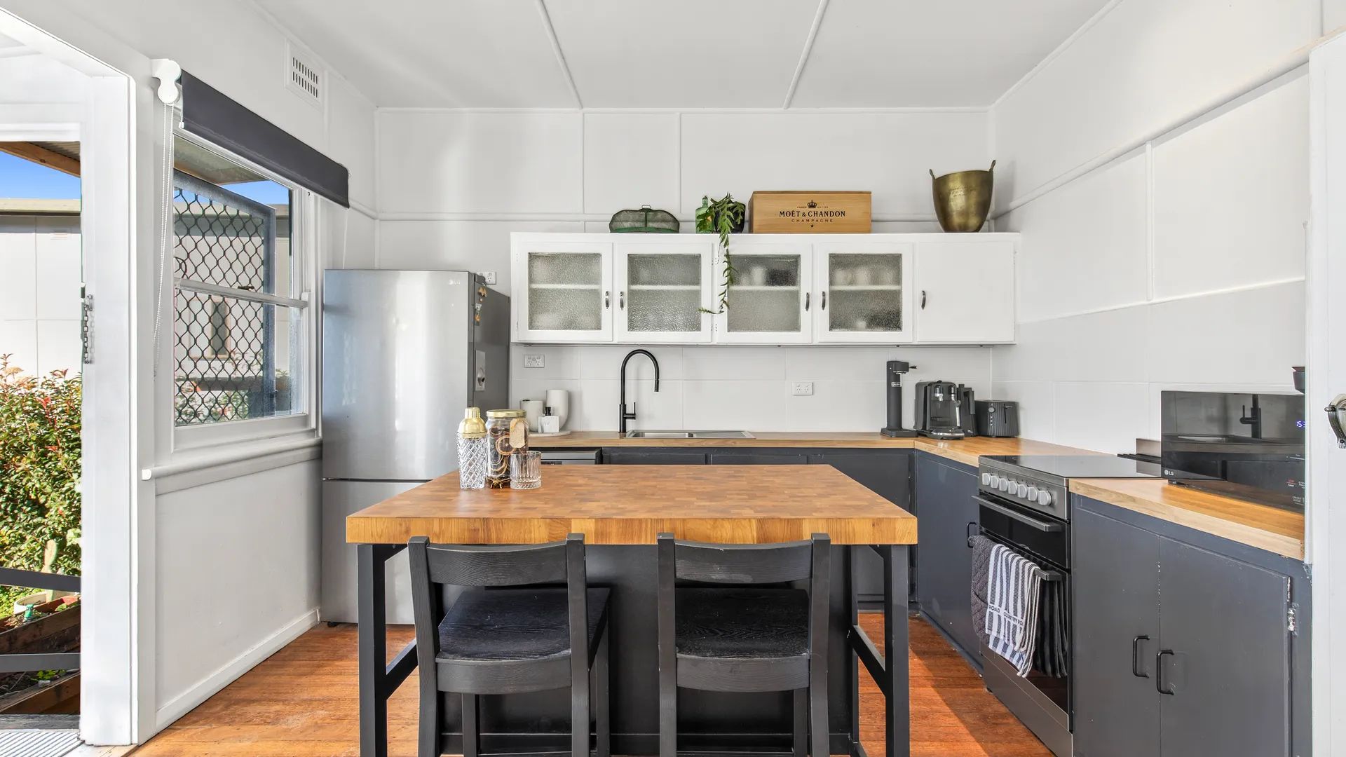 Une cuisine compacte avec une table en bois, deux chaises, un réfrigérateur, une machine à café et des placards avec des portes en verre.
