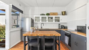 A compact kitchen with a wooden table, two chairs, a refrigerator, a coffee maker, and cabinets with glass doors.
