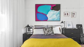 Une chambre à coucher moderne, avec un lit, des tables de chevet, une lampe et un grand tableau abstrait accroché au mur.
