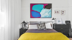 A modern bedroom with a bed, bedside tables, a lamp, and a large abstract painting on the wall.