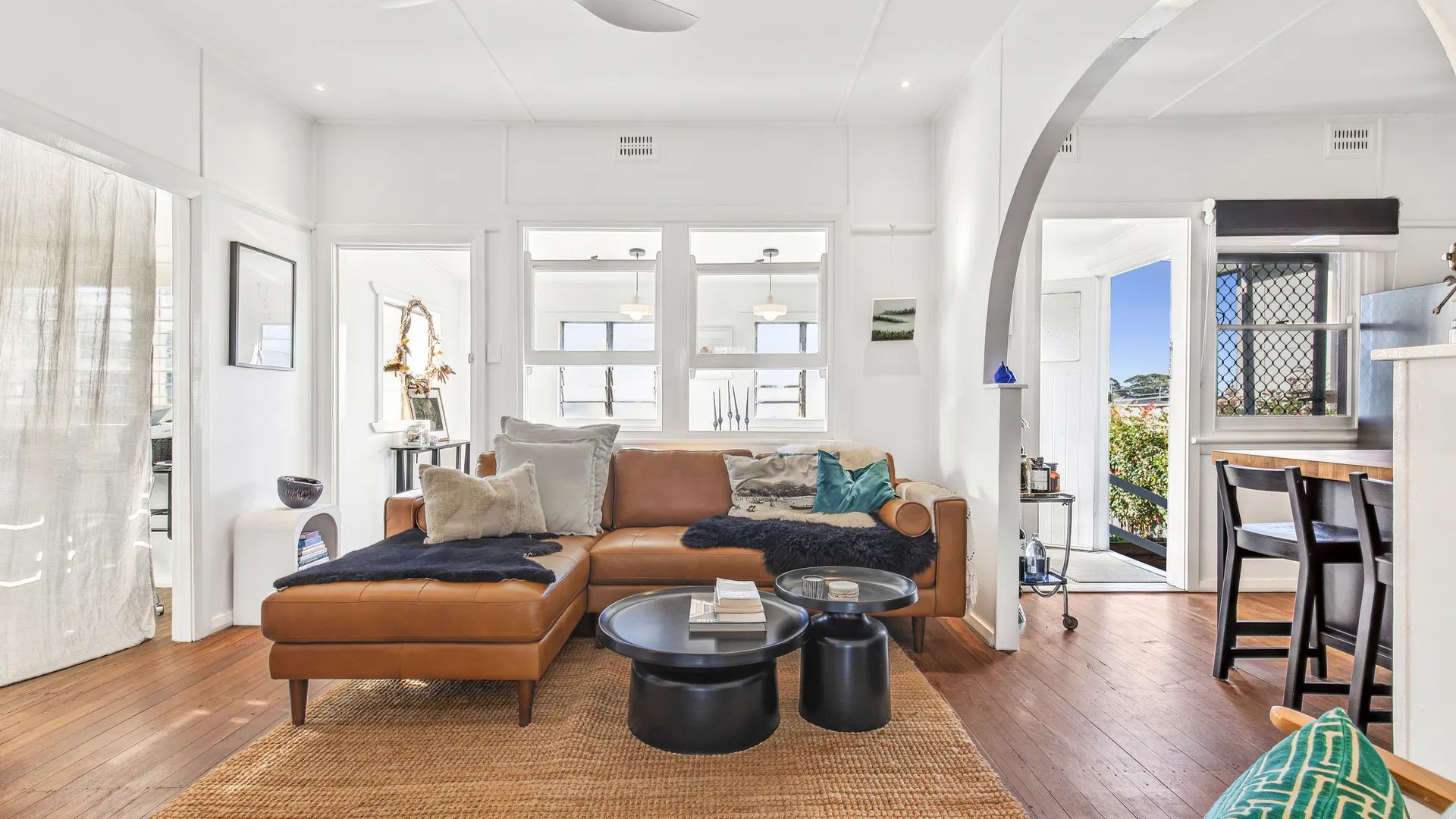 A spacious living room with a leather sofa, two coffee tables, and a view of the outdoors through large windows.