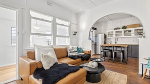 A modern living room with a leather sofa, a coffee table, and a view of a kitchen with white cabinets and a stainless steel refrigerator.