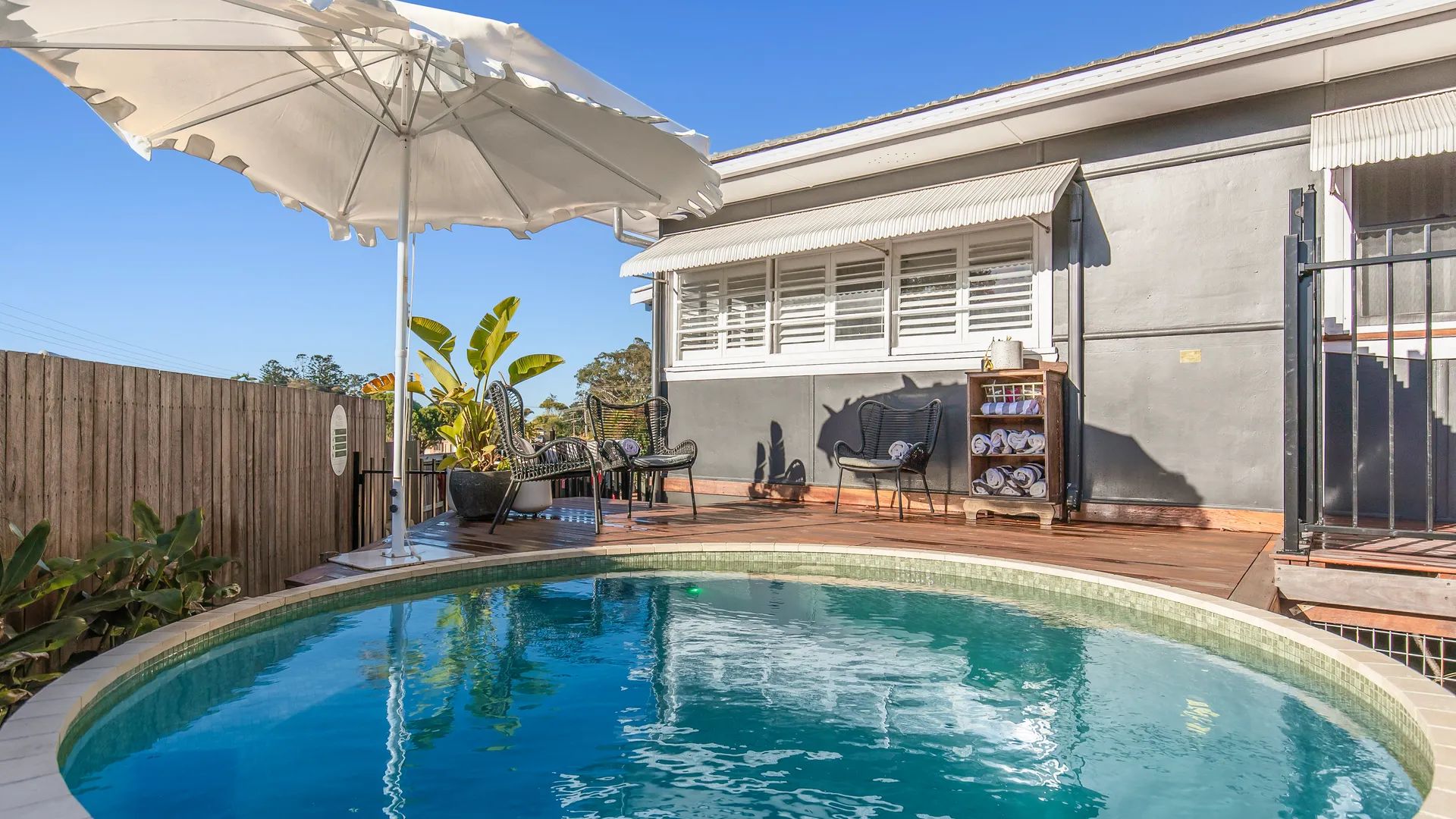 Une piscine avec une terrasse en bois, du mobilier d’extérieur et un espace salon abrité.