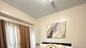 A bedroom with a bed, curtains, a painting, and a nightstand. - Kuya Awen’s Staycation 12H (Parañaque)