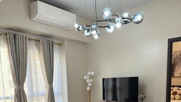 A modern living room with a sofa set, a flat-screen TV, a wooden cabinet, and a decorative light fixture. - Kuya Awen’s Staycation 12H (Parañaque)