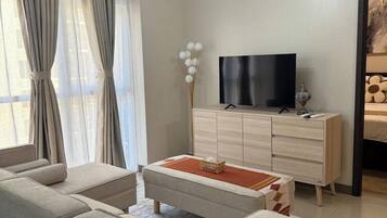 A modern living room with a sofa set, a flat-screen TV, a wooden cabinet, and a decorative light fixture.