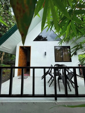 A white building with a wooden door and windows, surrounded by greenery.
