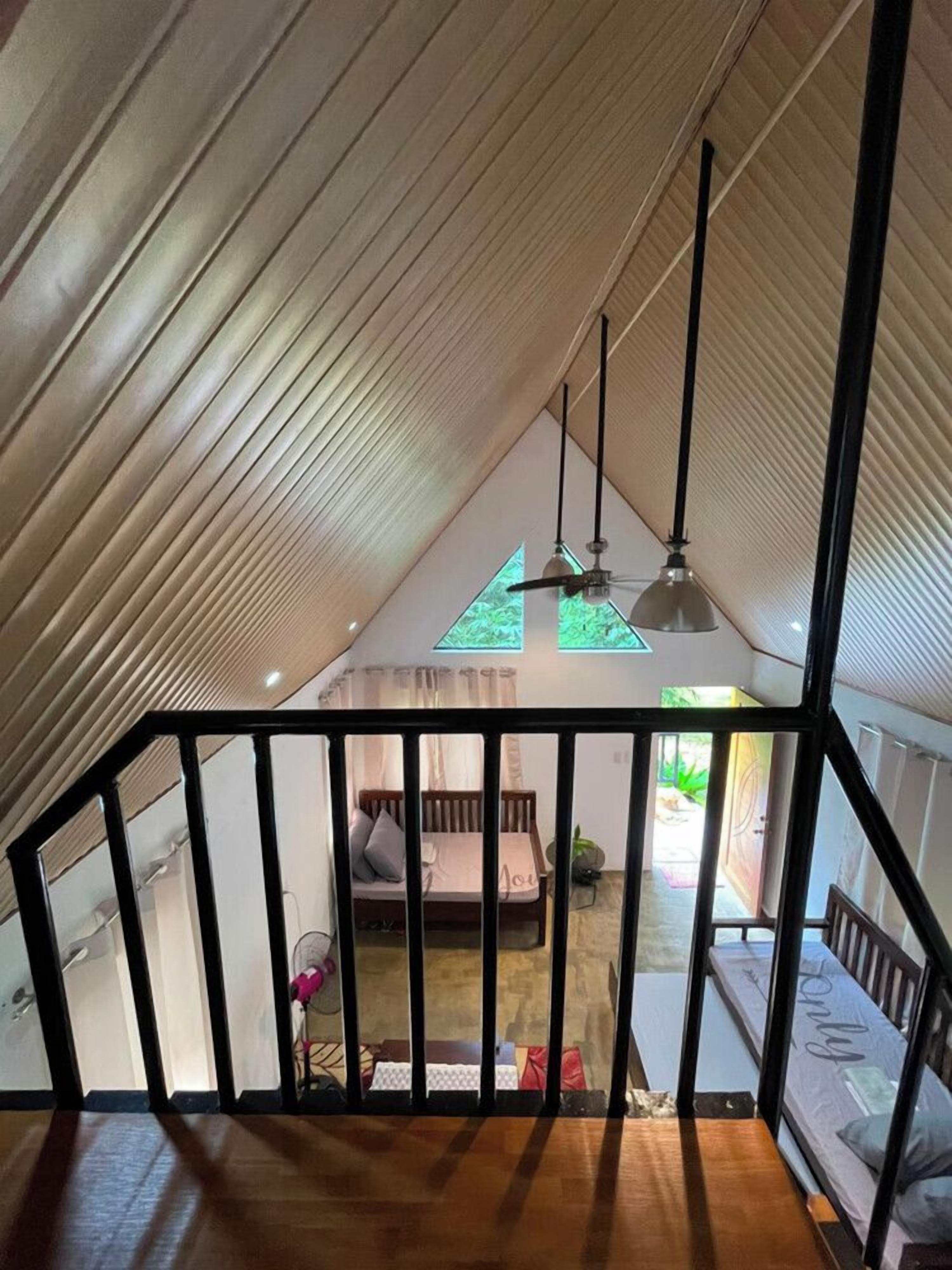 Um quarto com pé-direito alto e teto inclinado, escada com grades pretas e cama com cabeceira branca.