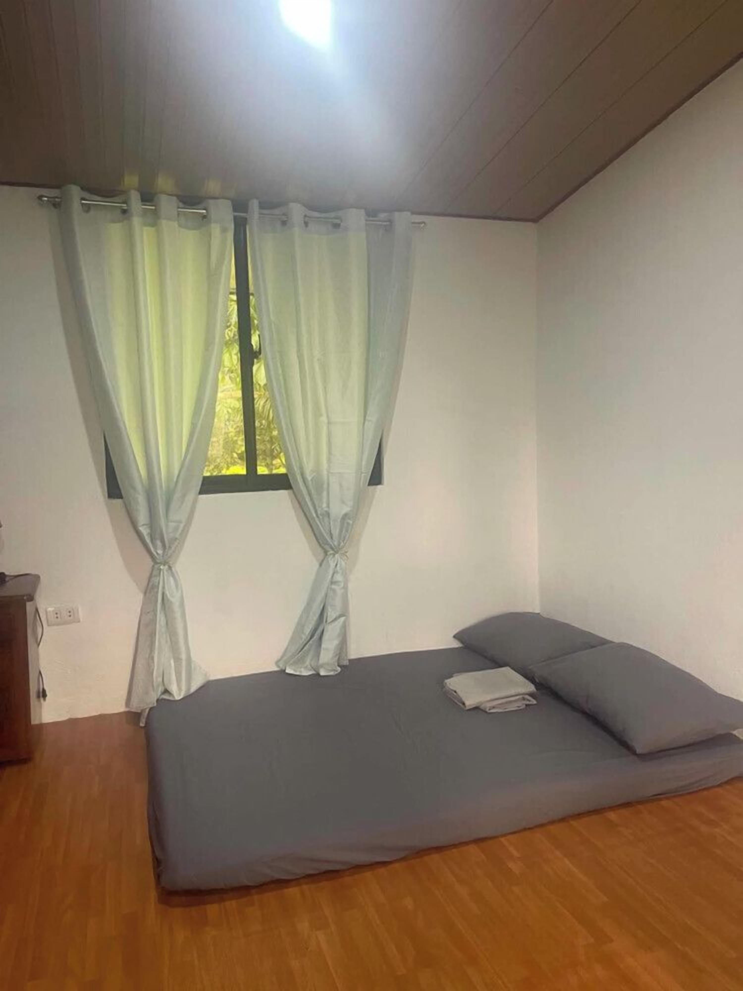 Een kamer met een enkel bed, een raam met gordijnen en een houten vloer.