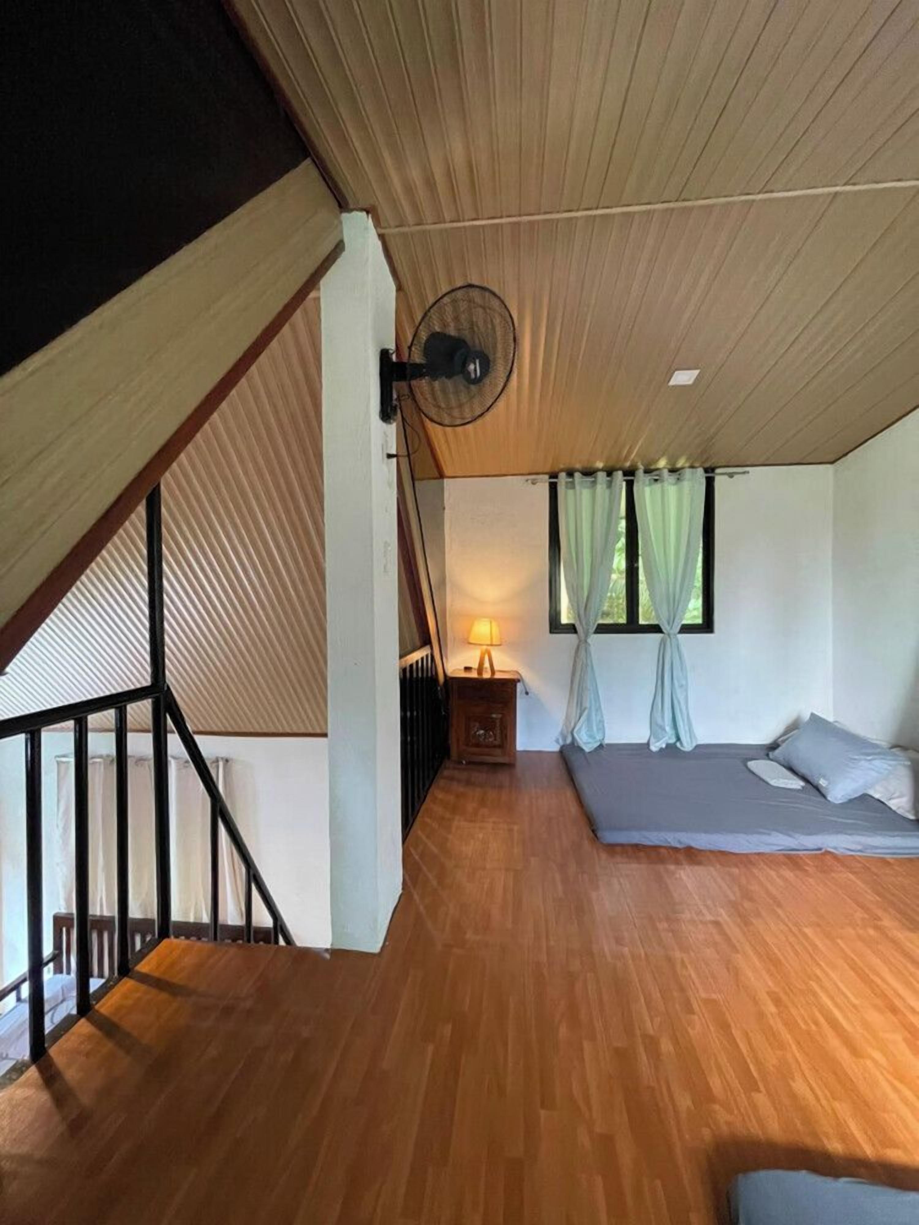 Una camera da letto con soffitto spiovente, un letto, un comodino, una lampada e una finestra con tende.