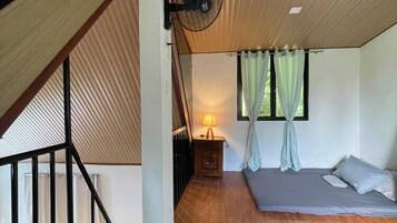 Una camera da letto con soffitto spiovente, un letto, un comodino, una lampada e una finestra con tende.