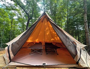 A dome-shaped tent with a table and chairs inside, set up in a forest.