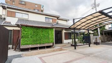A residential building with a traditional tiled roof, a covered outdoor area with a metal roof, and a green wall with climbing plants.
