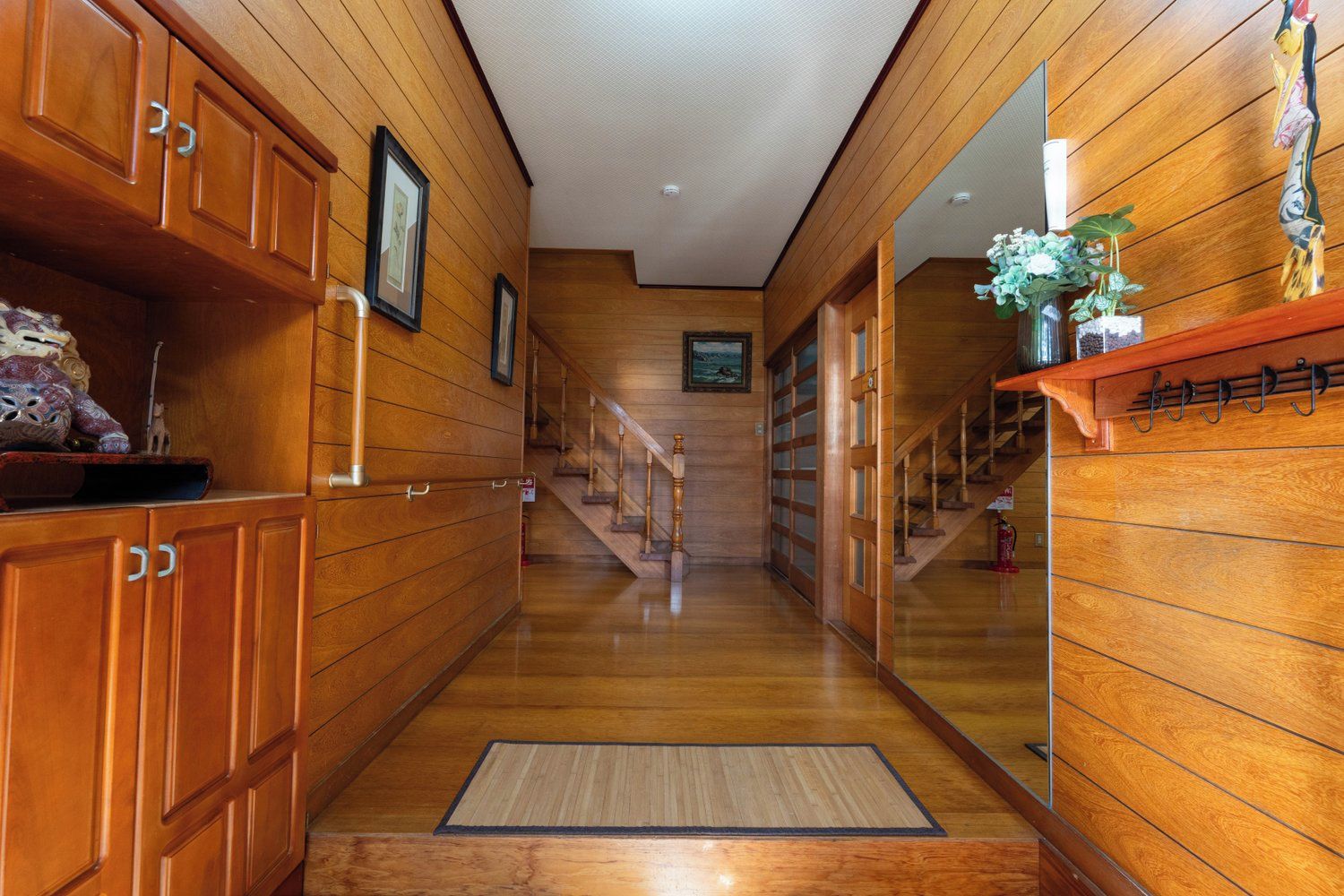 A wooden interior hallway with a polished floor, wooden cabinets, and a staircase leading to another level.