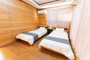 A room with two single beds, wooden panel walls, a ceiling fan, and a window with curtains.