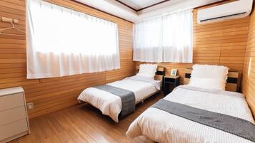 A hotel room with two beds, wooden panel walls, a white wardrobe, and an air conditioning unit.