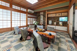 A traditional Japanese-style room with tatami flooring, a low table, cushions, and a television.
