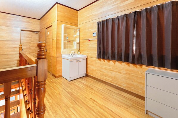 A wooden-floored bathroom with a white sink, a mirror, and a dark curtain.