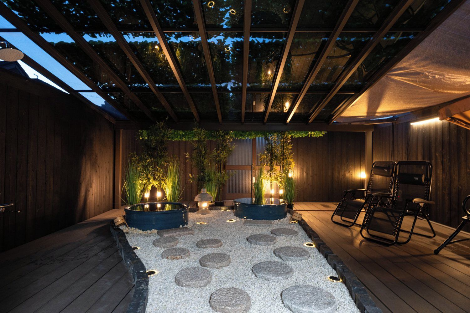 An outdoor patio area with a wooden deck, two hot tubs, and seating chairs.