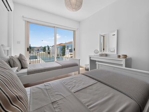 Een moderne slaapkamer met een groot raam, een bed, nachtkastje en uitzicht op een zwembad en gebouwen.