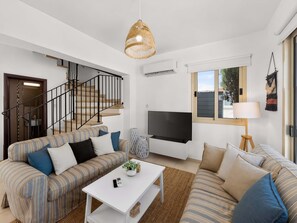 A modern living room with a staircase, a flat-screen TV, and a large window. - Villa Andreas: Private Pool & Modern Comfort (Protaras)