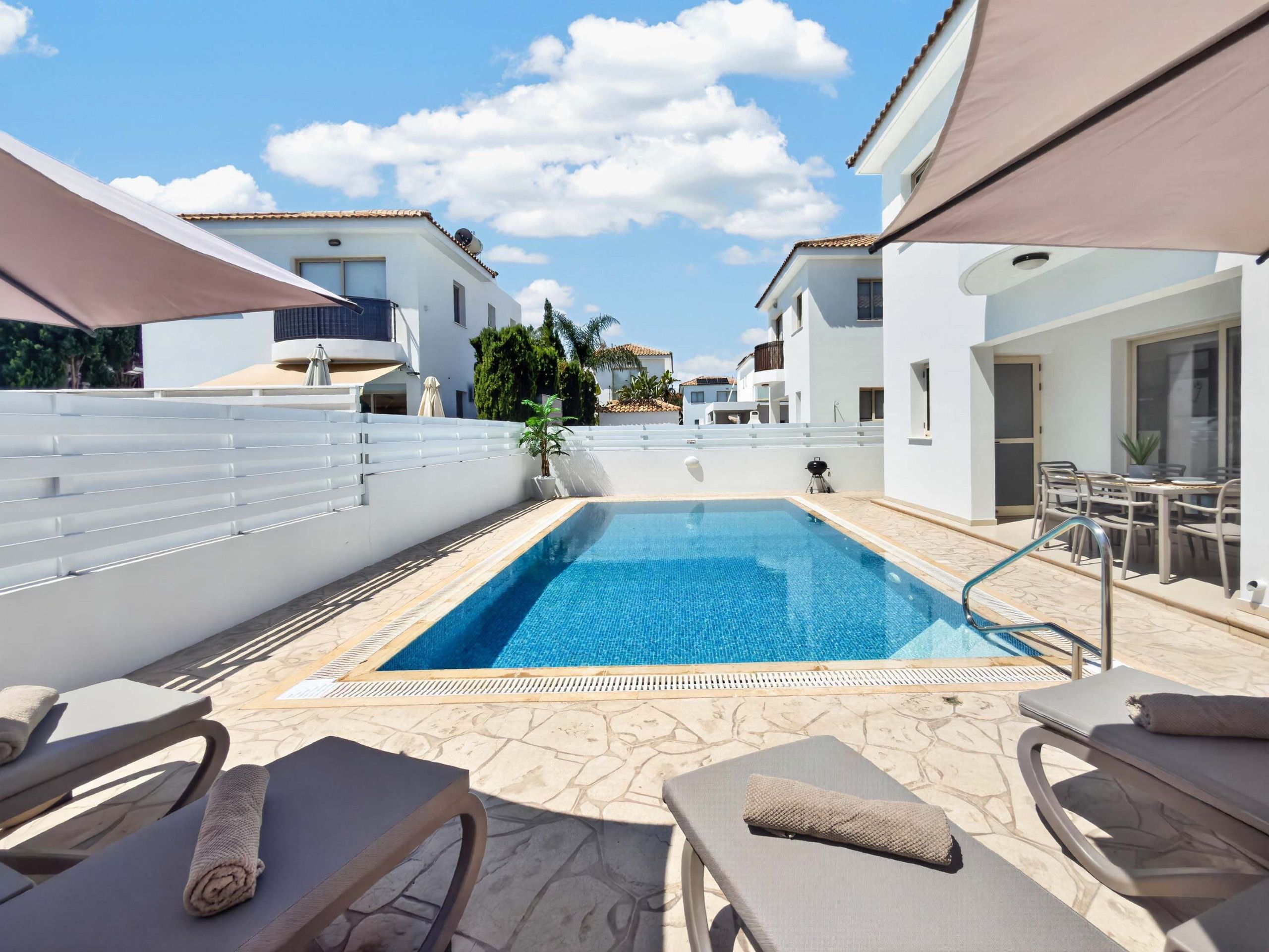 A swimming pool with lounge chairs and umbrellas, surrounded by white buildings.