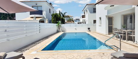 A swimming pool with lounge chairs and umbrellas, surrounded by white buildings.
