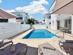 A swimming pool with lounge chairs and umbrellas, surrounded by white buildings. - Villa Andreas: Private Pool & Modern Comfort (Protaras)