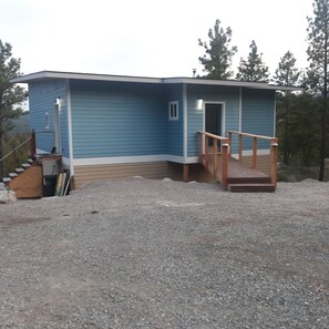 A small, single-story building with a wooden deck and a staircase leading to a door. - Sweet Somers one bedroom+home with outstanding views above Flathead Lake. (Somers)