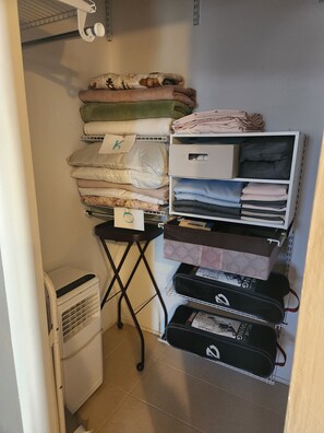 A storage area with shelves holding folded blankets and pillows, a small table with a box, and a suitcase on the floor. - Sweet Somers one bedroom+home with outstanding views above Flathead Lake. (Somers)