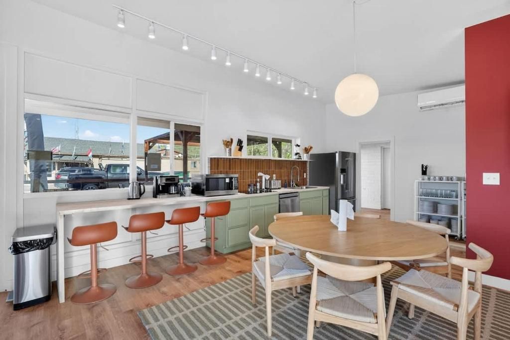 A modern kitchen with bar stools, a dining table, and a view of the outside.