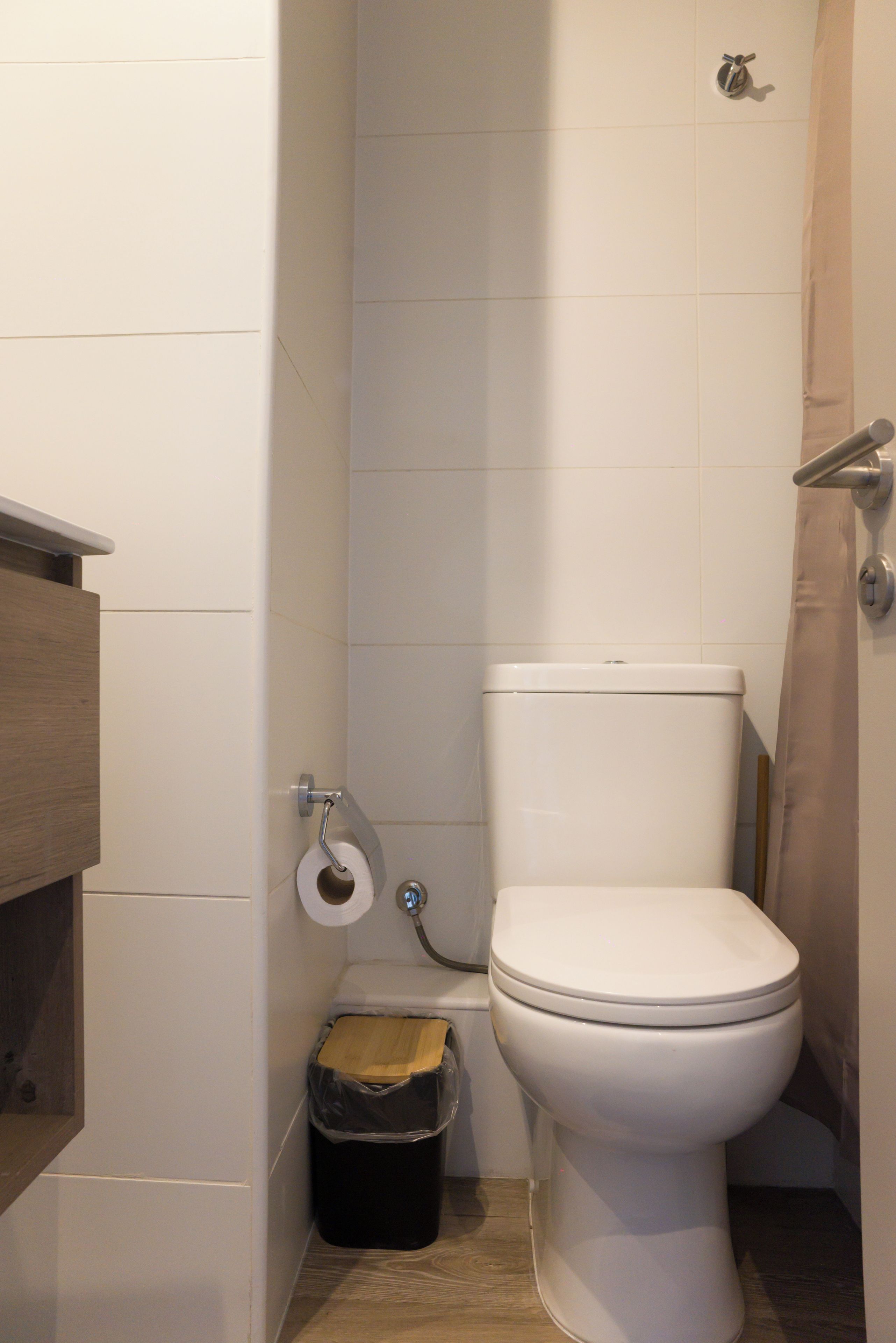 Un baño pequeño y funcional con inodoro, un cesto de madera y un rollo de papel higiénico en la pared.