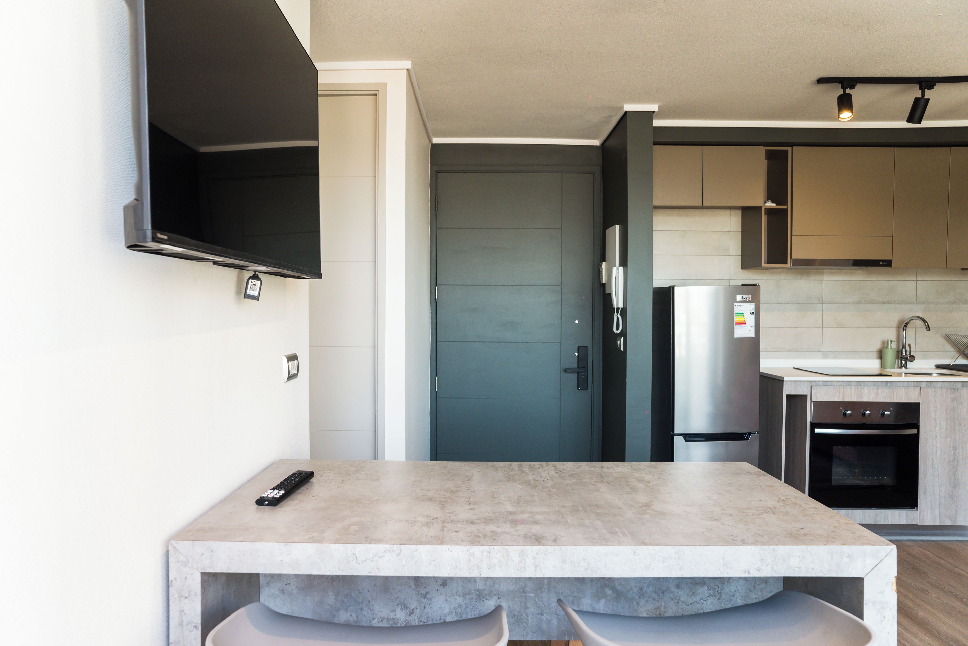 Eine moderne Küche mit Backofen, Kühlschrank und Mikrowelle. Ein Esstisch mit Stühlen und einer Fernbedienung steht daneben.