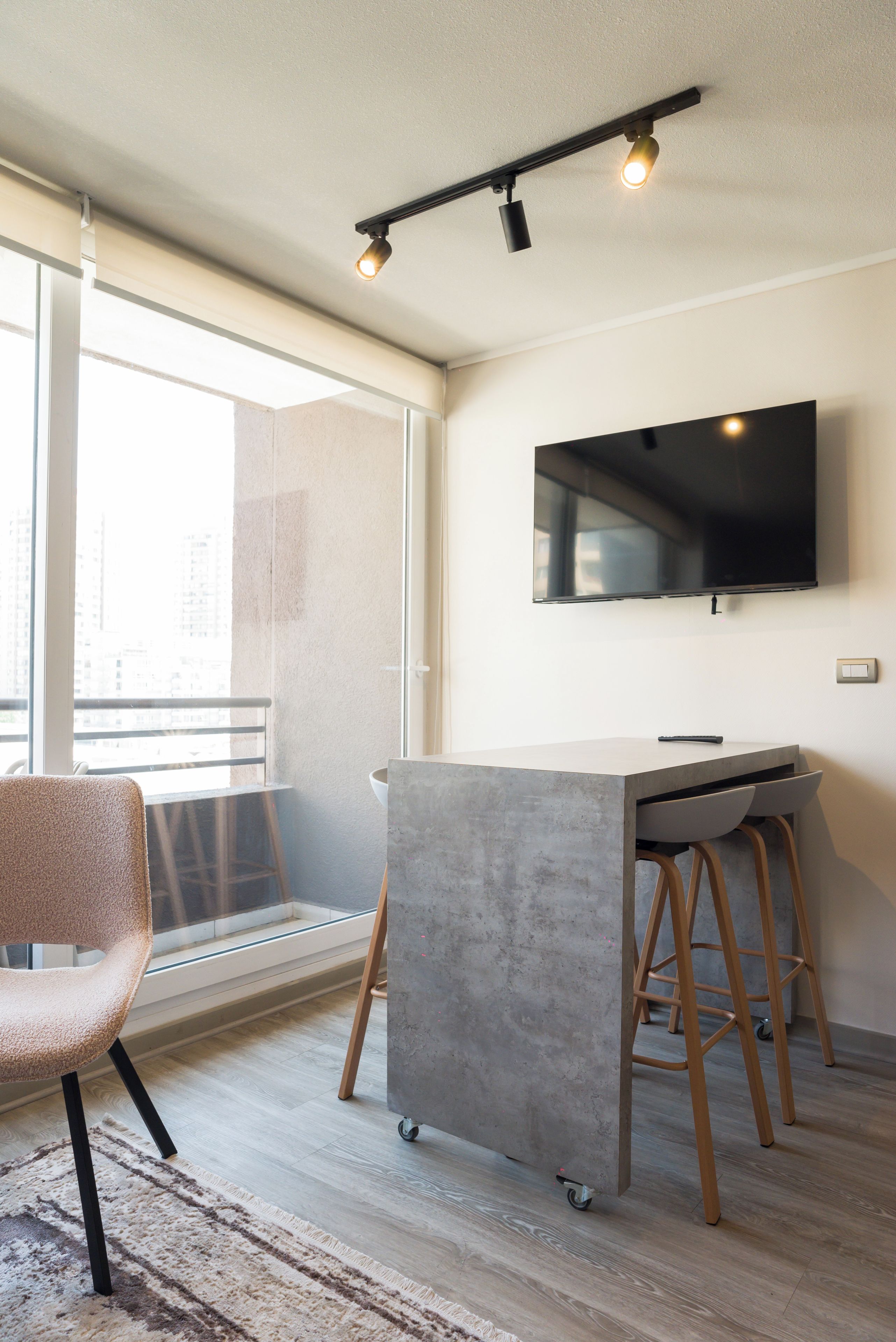 Ein modernes Wohnzimmer mit großem Fenster, einem an der Wand befestigten Flachbildfernseher, einer Bar mit Hockern und einem Sessel.