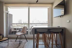 A modern apartment with a balcony, a dining area with bar stools, and a flat-screen TV mounted on the wall. - Chic 2BR Apt in Ñuñoa with Balcony for 5 (Ñuñoa)