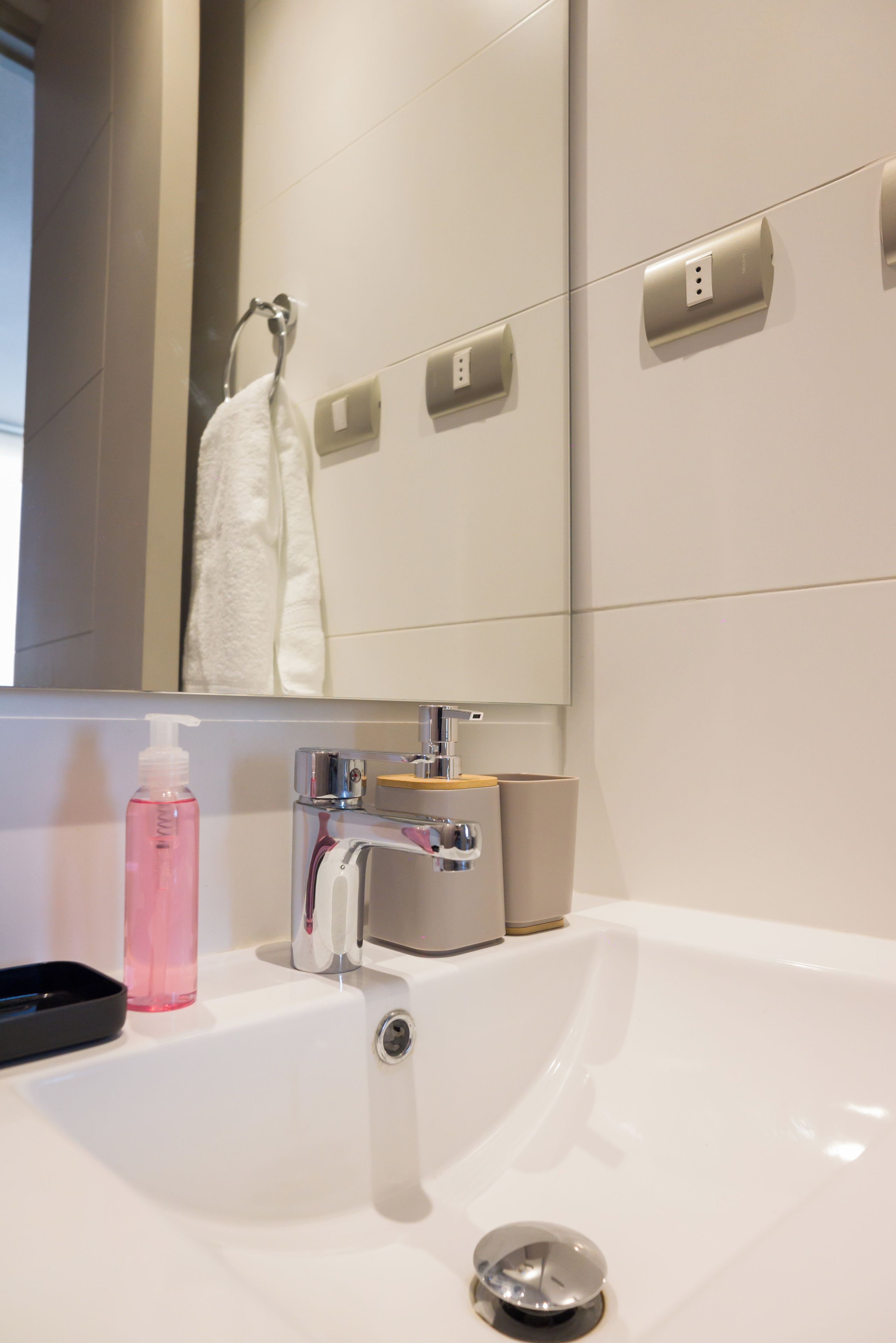 A bathroom with a white sink, a mirror, a towel, and a soap dispenser.