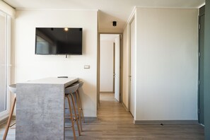 A modern kitchen with a large island, bar stools, a flat-screen TV mounted on the wall, and a hallway leading to another room. - Chic 2BR Apt in Ñuñoa with Balcony for 5 (Ñuñoa)