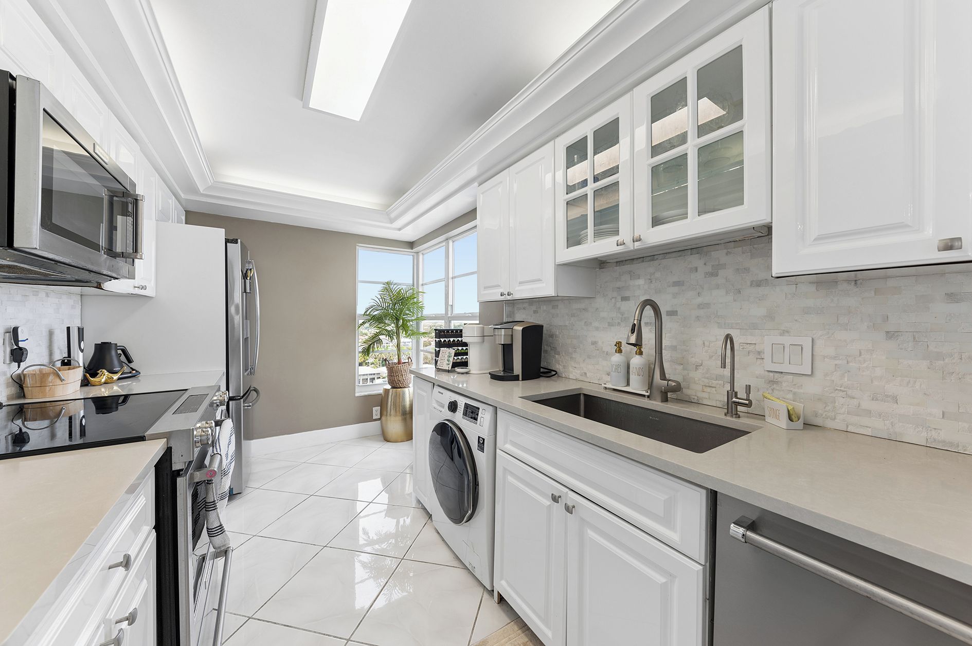 A modern kitchen with white cabinetry, a stainless steel refrigerator, and a built-in washing machine.
