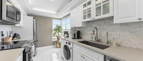 A modern kitchen with white cabinetry, a stainless steel refrigerator, and a built-in washing machine.