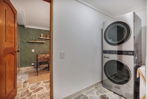A laundry room with two stacked washing machines, a wooden door, a stone floor, and a small table with a chair. - Peaceful 2-Bedroom Retreat in El Poblado (Medellín)