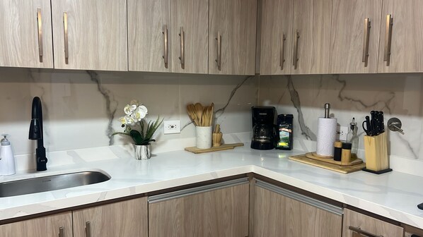 A kitchen with wooden cabinets, a marble countertop, a coffee maker, and a plant. - Peaceful 2-Bedroom Retreat in El Poblado (Medellín)