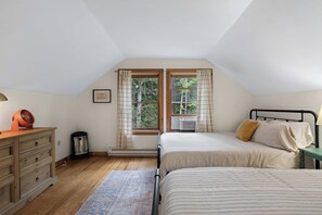 A bedroom with a bed, a dresser, a heater, and a window with curtains.