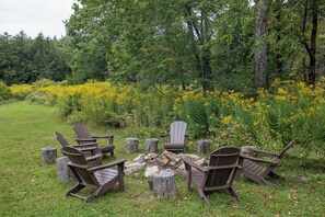 An outdoor seating area with Adirondack chairs and a fire pit surrounded by a natural landscape.
