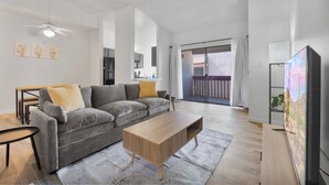 Uma sala de estar moderna com um sofá cinza, uma mesa de centro de madeira, uma televisão de tela plana e uma varanda com vista.