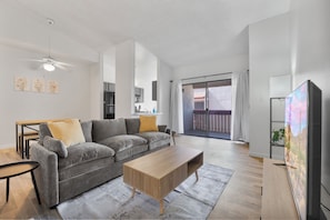 Een moderne woonkamer met een grijze bank, een houten salontafel, een flatscreen televisie en een balkon met uitzicht.