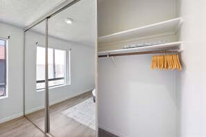 A room with a large window, a sliding glass door, and a closet with hanging clothes.