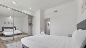 Quarto moderno com uma cama grande, porta de correr para o armário e vista para outro espaço.