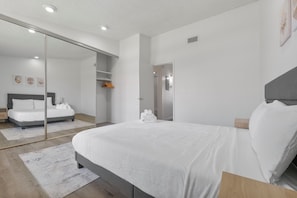 Een moderne slaapkamer met een groot bed, een schuifdeurkast en uitzicht op een andere kamer.
