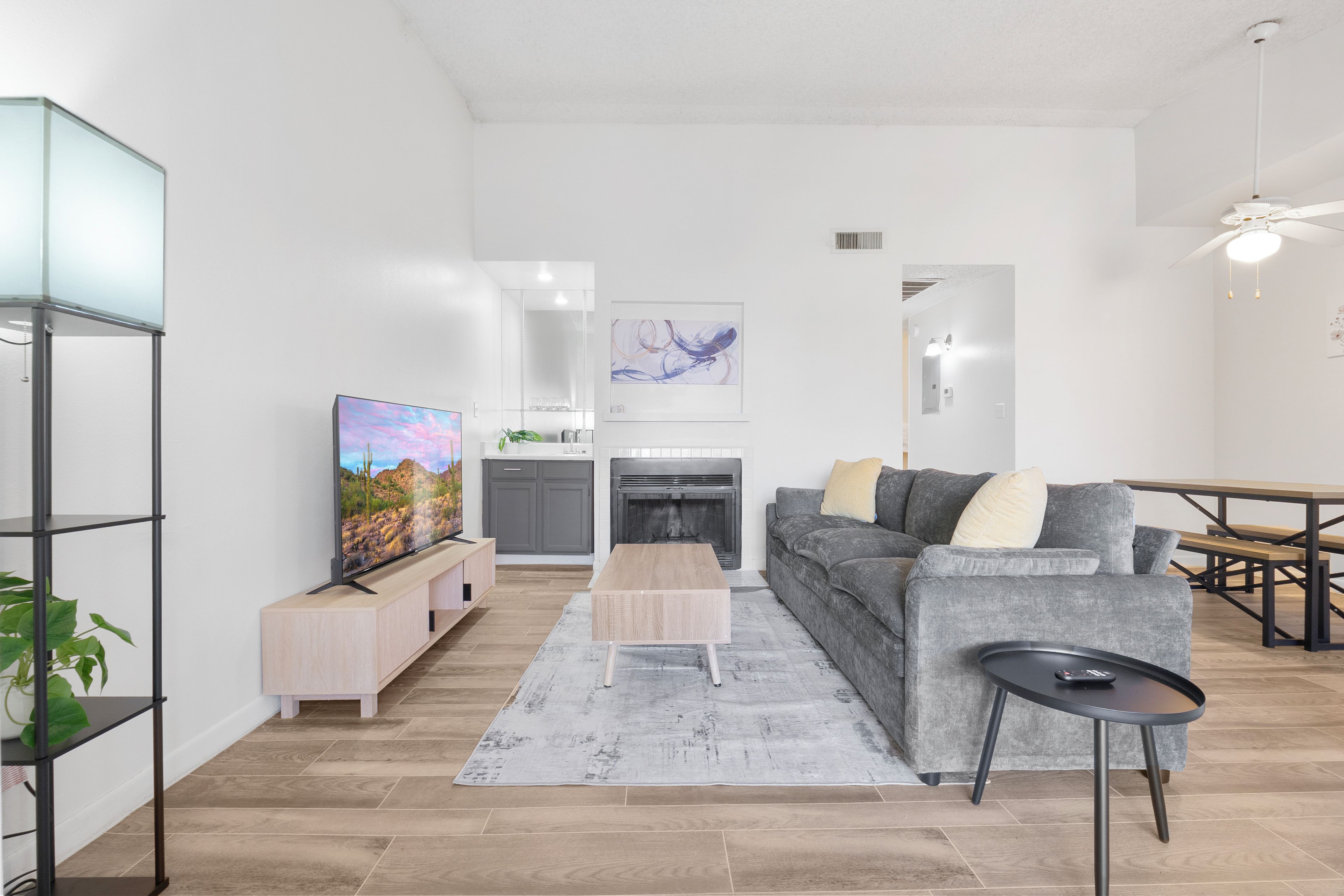 Ein modernes Wohnzimmer mit einem Flachbildfernseher, einem grauen Sofa, einem Couchtisch und einem Essbereich mit einem Holztisch und Bänken.